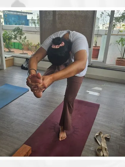 A student demonstrates the art of balance in a challenging standing forward bend, a physical manifestation of the inner alignment we cultivate at Aikia.