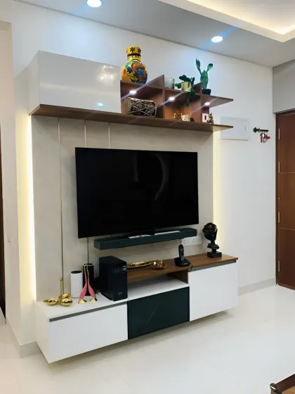 A practical and stylish TV unit design featuring a mix of open and closed storage. The white and wood laminate finish is complemented by accent lighting, creating a modern focal point.