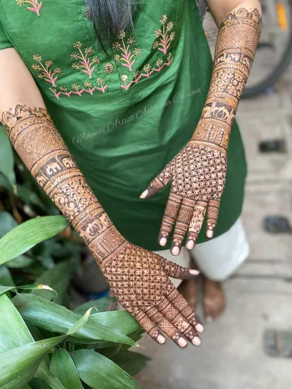 A back-of-the-hand view of a full bridal mehendi. The design features checkerboard patterns and personalized initials, extending all the way up the arms.