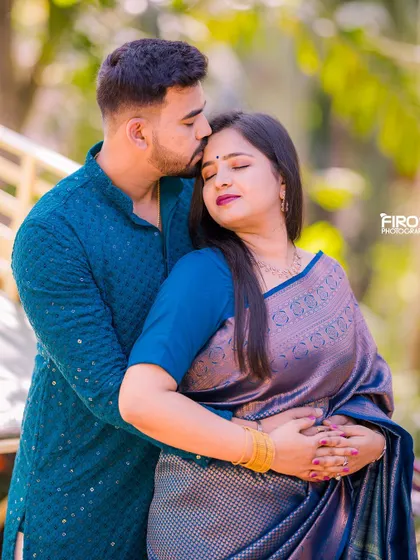 A sweet forehead kiss, capturing a tender moment between the couple. Their elegant blue traditional outfits add to the romantic feel of the photo.