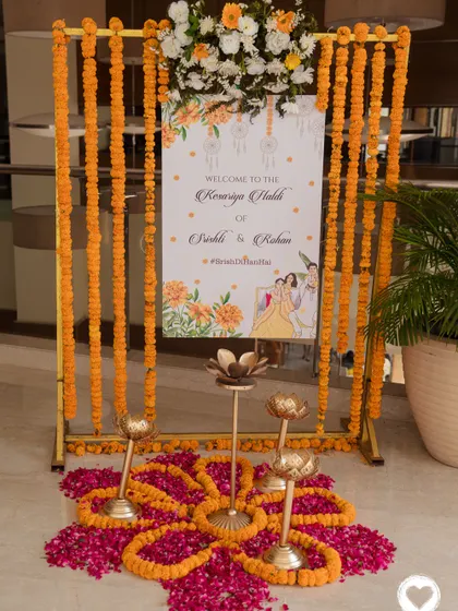 An elegant welcome sign for the "Kesariya Haldi" ceremony, framed by marigold garlands and traditional brass diyas on a bed of rose petals.