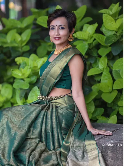 A relaxed and smiling portrait in a green saree, taken outdoors against a lush, natural backdrop.