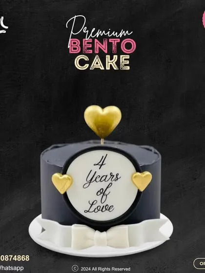 "4 Years of Love." This elegant black bento cake is a beautiful way to mark an anniversary. It's adorned with gold hearts and a delicate white bow for a touch of class.