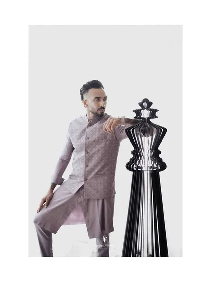 An artistic portrait of the groom in a lavender kurta set, posing next to a large chess piece, symbolizing a strategic and thoughtful personality.