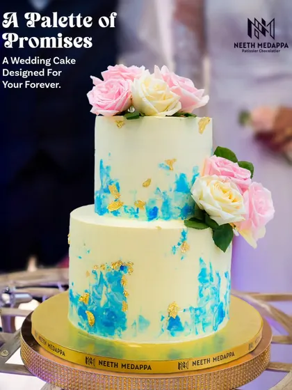 A palette of promises. This two-tiered wedding cake features a beautiful blue watercolor design on a pale yellow canvas, accented with gold leaf and fresh roses.