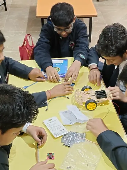A team of four students works together at a table to assemble their first robotic vehicle, learning about teamwork and mechanical design.