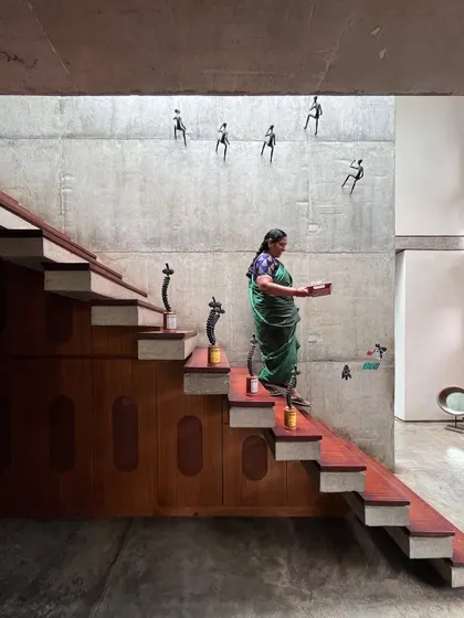 The central staircase at Nirvana Films is more than just for circulation; it's a sculpture of wood and concrete bathed in natural light from a skylight above. The wall art depicting human figures in motion adds a dynamic layer to the space, celebrating the creative energy within.