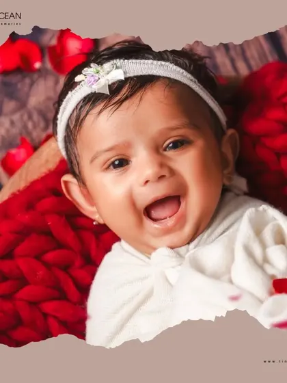 The purest joy in a single frame. This close-up from a newborn session highlights that beautiful, gummy smile, framed by a soft red knit blanket and delicate rose petals for an artistic and tender portrait.