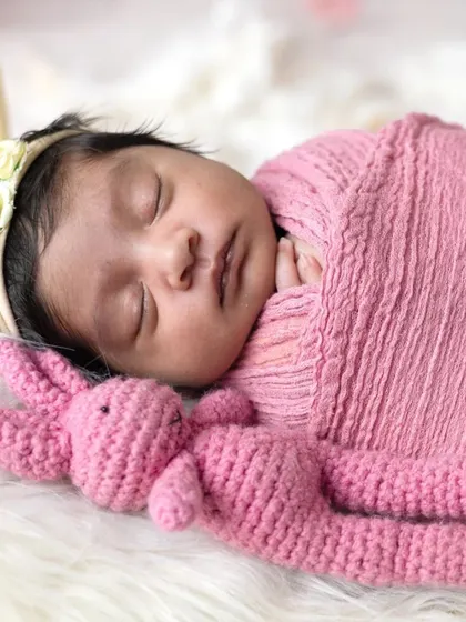 Sleeping soundly in a miniature bed, this newborn is surrounded by soft pink flowers. These styled setups create beautiful, dreamy portraits.