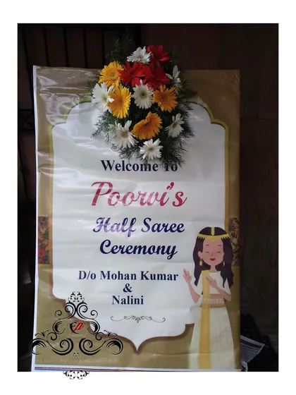 A personalized welcome board for a half-saree ceremony. The design includes a cute illustration and a fresh flower arrangement at the top.
