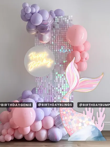 A chic and modern mermaid theme with a pastel purple and pink shimmer wall. A neon "Happy Birthday" sign and a large, iridescent mermaid tail cutout make this a stylish and eye-catching design.