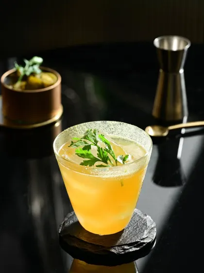 The Wildcat of Bombay, a golden-hued drink served in a modern, conical glass with a fresh parsley garnish.