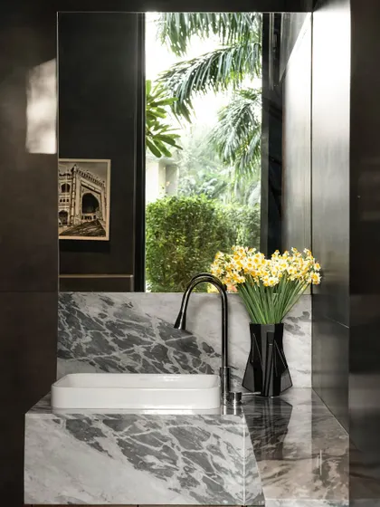 Even small spaces like a powder room can tell a story. Here, a custom marble vanity with a waterfall edge is set against a large mirror that reflects the lush greenery outside, making the room feel connected to nature.