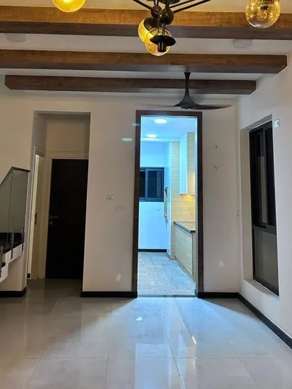 An empty living room in a duplex villa, showing the staircase, the view into the kitchen, and the beautiful wooden ceiling beams. This is the foundational quality upon which we build your dream home.