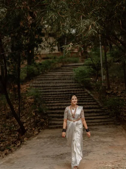 A full-length shot of a South Indian bride walking along a path surrounded by lush greenery. This image captures the bride's grand entrance with a sense of serenity.