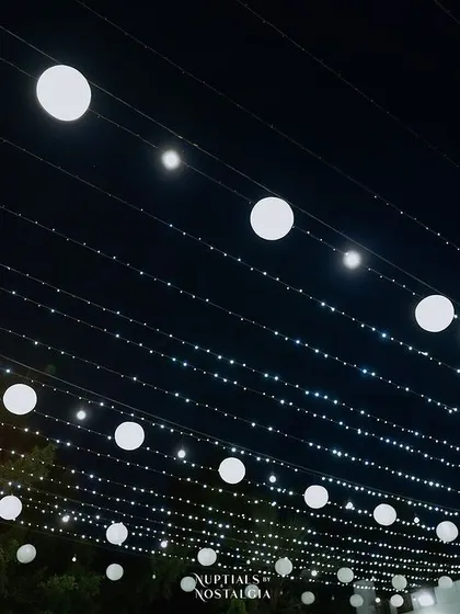 A canopy of fairy lights and paper lanterns illuminates the night sky, creating a magical and festive atmosphere for the Sangeet.