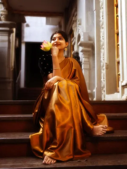 A dreamy, artistic shot in a gold satin saree, seated on temple steps. The lotus flower adds a touch of symbolism and beauty to this ethereal portrait.