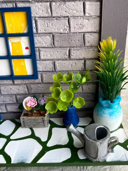 A detail shot of the 'Chilakalas' nameplate, focusing on the miniature plants and watering can. I use a mix of materials to create a lush, tiny garden scene.