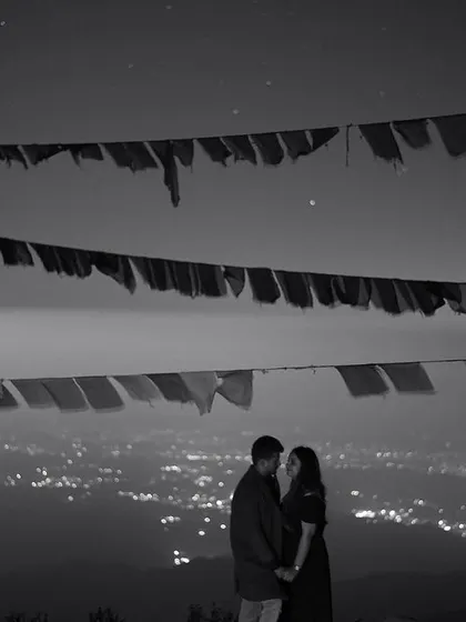 A stunning black and white shot of a couple against the backdrop of Mussoorie's city lights at night. The Tibetan prayer flags add a beautiful textural element to this dramatic and romantic nightscape.