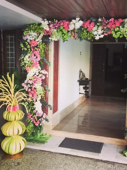 A beautiful floral arch at the entrance of a home, combining modern flowers with traditional leaf decorations.