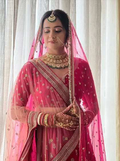 A full-length portrait of the bride, showcasing the beautiful drape of her sheer pink dupatta over the lehenga.