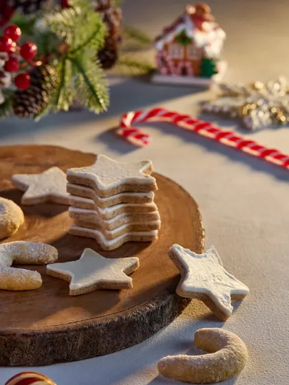 A lovely shot of star-shaped and crescent Christmas cookies on a rustic wooden board. The soft, warm lighting and festive decorations in the background create a gentle and inviting holiday mood for this Marriott Bonvoy shoot.