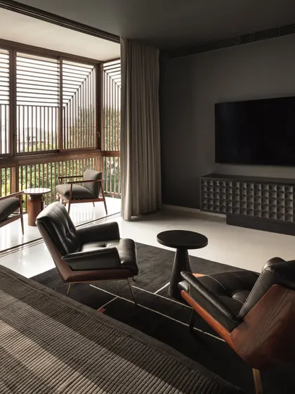 This media room combines moody, dark tones with a bright, airy balcony screened by timber lattices. It serves as a private retreat that can be opened up to natural light and ventilation.
