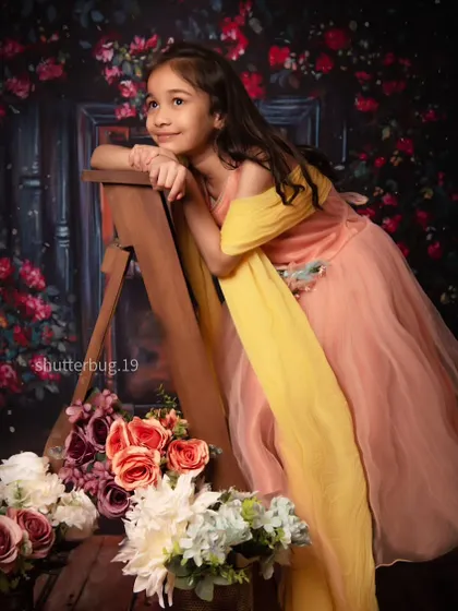 A graceful portrait of a young girl in a beautiful peach gown, posing against a romantic floral backdrop.