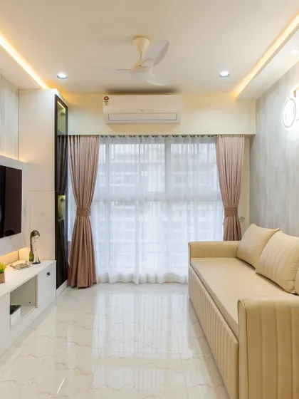 A bright and neutral living room with a simple false ceiling and profile lighting. The design focuses on creating a sense of spaciousness and calm.