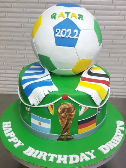 Celebrate the beautiful game with this Qatar 2022 World Cup theme cake. It features a sculpted soccer ball on top, team flags, and the iconic trophy, making it the perfect cake for any football fan.