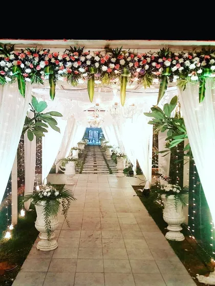 To welcome guests, I designed this enchanting entrance pathway for an outdoor wedding. The walkway is lined with elegant white drapes, fairy lights, and lush floral arrangements in classic urns, leading to a beautifully lit water feature in the distance.