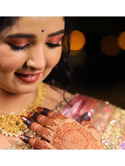 A close-up shot focusing on the bride's intricate henna design and her serene expression. The bokeh in the background adds a touch of magic.