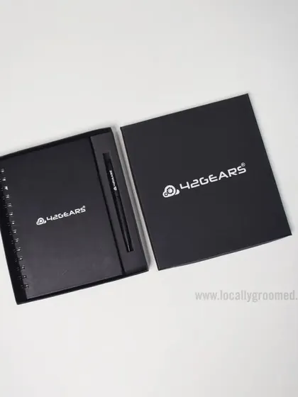A classic and professional gift set for 42Gears. This includes a black spiral notebook and a matching pen, presented in a sleek box with the company's logo prominently displayed.