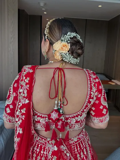The final look of the peach rose and baby's breath bun, paired with a red lehenga. The back view shows the neatness of the bun and the beautiful contrast of the flowers.