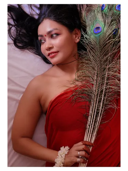 An artistic portrait featuring a peacock feather. The composition and the subject's expression create a sense of connection to nature and a quiet, meditative mood.