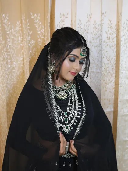 A model in a black outfit, showcasing a grand layered AD and emerald necklace set.