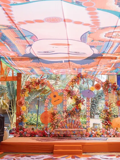A vibrant, Mexican-themed Mehendi setup. The decor is full of color, with a custom printed ceiling, floral arches, and quirky elements like a guitar prop, creating a true fiesta atmosphere.