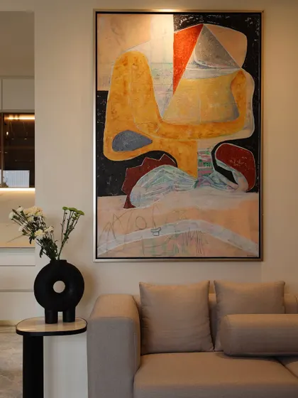 A closer view of the living room corner, where the bold brushstrokes and colors of the abstract painting are the clear hero. The minimal furniture and neutral wall color are intentionally chosen to let the artwork speak.