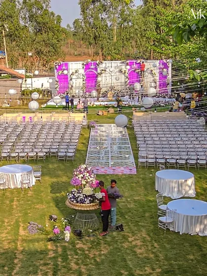 An overhead view of an outdoor wedding setup in progress. This shot shows the scale of our work, from the guest seating arrangement to the grand stage and the unique floral-filled glass aisle.