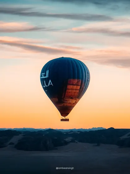 A hot air balloon floats over the Al Ula desert at sunrise. This image captures the serene and magical experience of the 'Al Ula Skies' festival, a key attraction for visitors to the region.