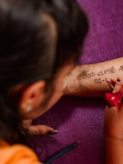 A close-up of a father getting his daughter's wedding date written on his arm in henna. A beautiful, personal gesture of love.