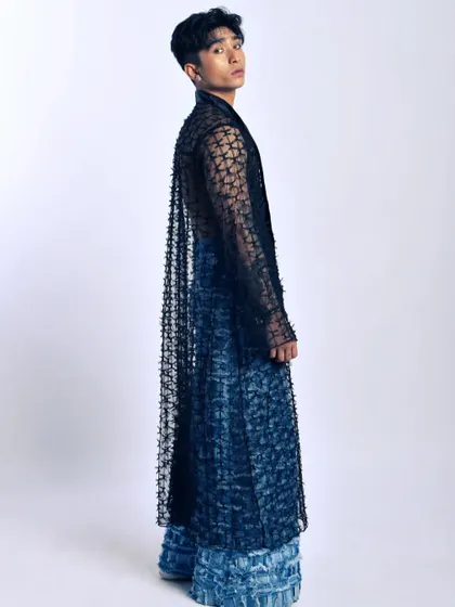 A dramatic full-length shot. The long, sheer coat adds a sense of movement and theatricality to the entire outfit.