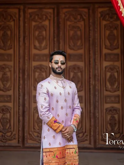 This is a closer look at a bespoke sherwani I crafted from Paitani silk. The soft lavender color is complemented by traditional motifs along the hem and cuffs, making it a standout piece for a groom who values classic elegance.