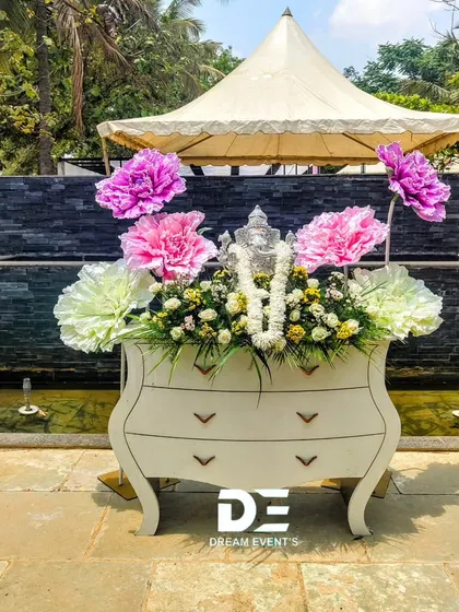 A unique and creative decor piece for an outdoor event. I used a vintage-style dresser as a base for a large floral arrangement featuring oversized paper flowers and a small Ganesha idol, creating a quirky and artistic photo op.