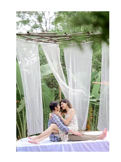 A dreamy and romantic pre-wedding setup in a lush, green location. The flowing white curtains and natural light create a soft, ethereal vibe for this couple's portrait.