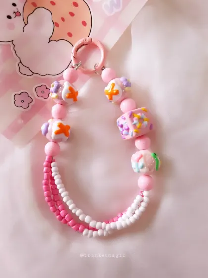 This image showcases the pink cake-bead charm against a cute, illustrated background, emphasizing its playful and kawaii aesthetic.