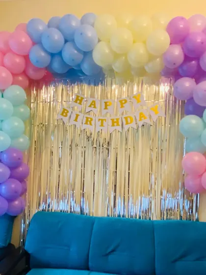 A simple pastel rainbow balloon arch set against a silver foil curtain, perfect for a colorful home birthday celebration.