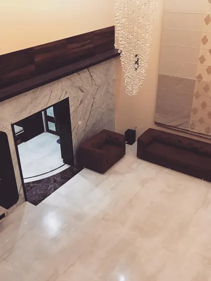 An aerial view of the double-height living room in a Hubli bungalow. This perspective shows the grand scale of the space, the marble flooring, and the placement of furniture to create an intimate seating area under the cascading crystal chandelier.