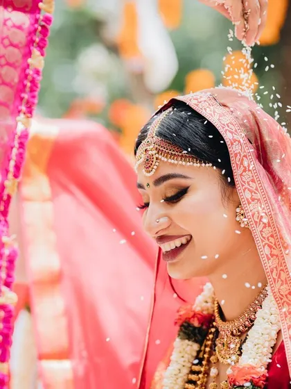 A bride smiles blissfully as rice grains, a symbol of prosperity and blessings, are showered over her during the ceremony.