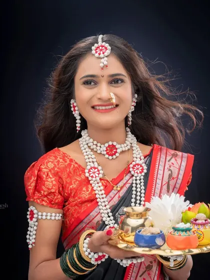 A classic studio portrait of a woman in traditional Makarsankranti attire, holding a thali with small decorative pots. The clean, dark background makes the colors of her outfit pop.